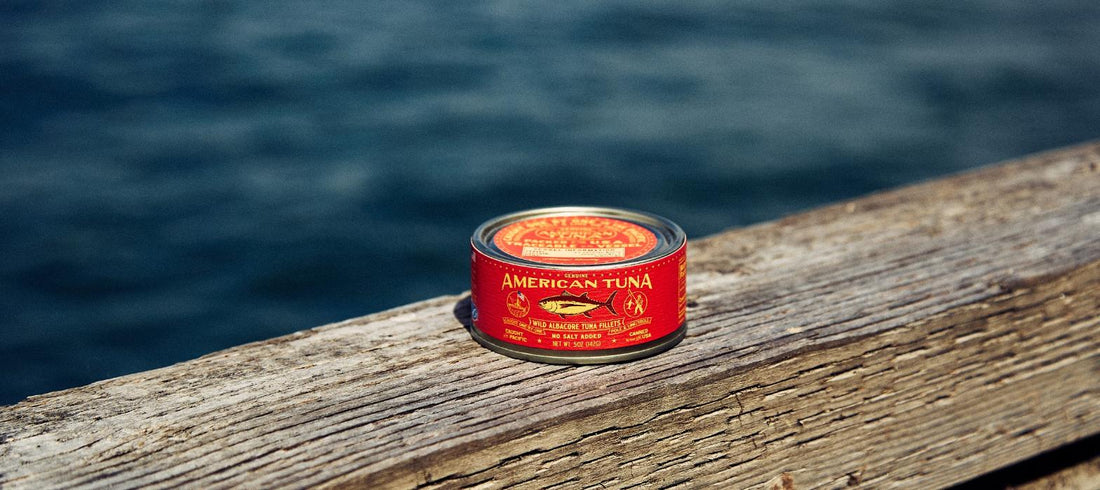 Can of wild albacore tuna fillets resting on a weathered dock rail above the water