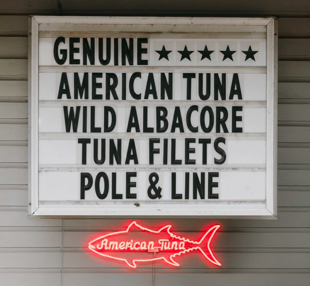 Sign reading ‘Genuine American Tuna Wild Albacore Tuna Filets Pole & Line’ next to a glowing neon tuna fish sign.