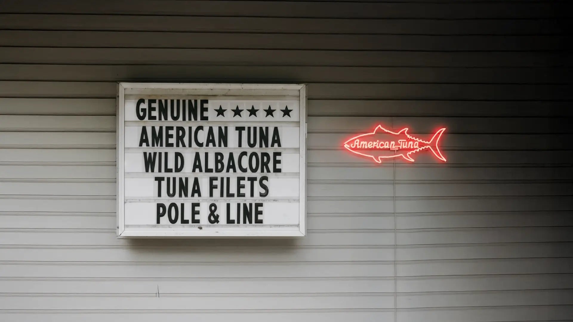 Sign reading ‘Genuine American Tuna Wild Albacore Tuna Filets Pole & Line’ next to a glowing neon tuna fish sign.